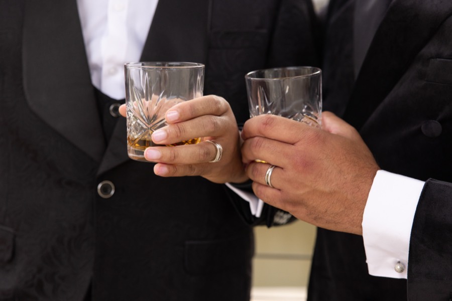 Two hands with engagement rings holding crystal glasses of bourbon